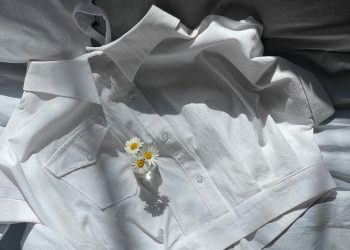 a white shirt laying on top of a bed next to a flower