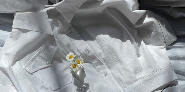 a white shirt laying on top of a bed next to a flower
