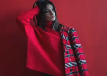 woman holding her head wearing red long-sleeved shirt and half of coat