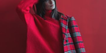 woman holding her head wearing red long-sleeved shirt and half of coat
