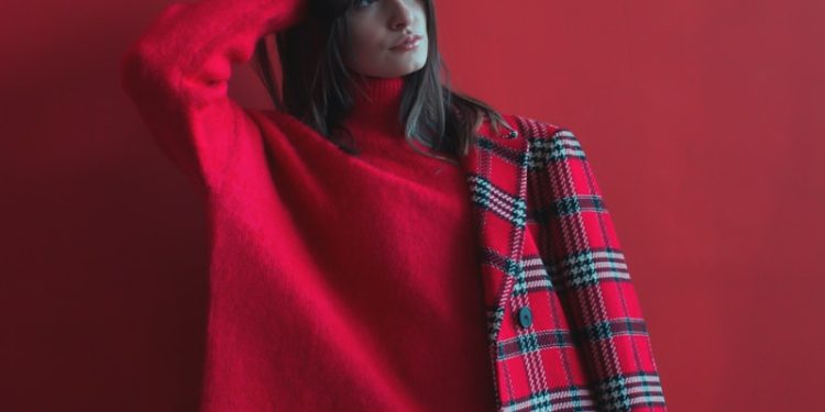 woman holding her head wearing red long-sleeved shirt and half of coat