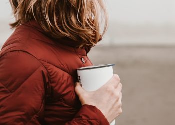 woman wearing brown bubble jacket holding white disposable cup