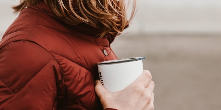 woman wearing brown bubble jacket holding white disposable cup