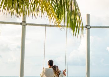 man in white shirt sitting on swing chair under coconut tree during daytime