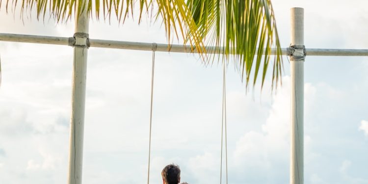 man in white shirt sitting on swing chair under coconut tree during daytime