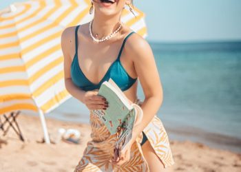 smiling woman in blue brassiere kneeling on white textile on shore during daytime