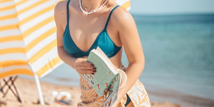smiling woman in blue brassiere kneeling on white textile on shore during daytime